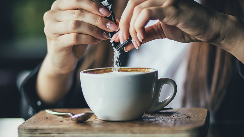 The girl's hand pours sugar into her coffee. Close up.